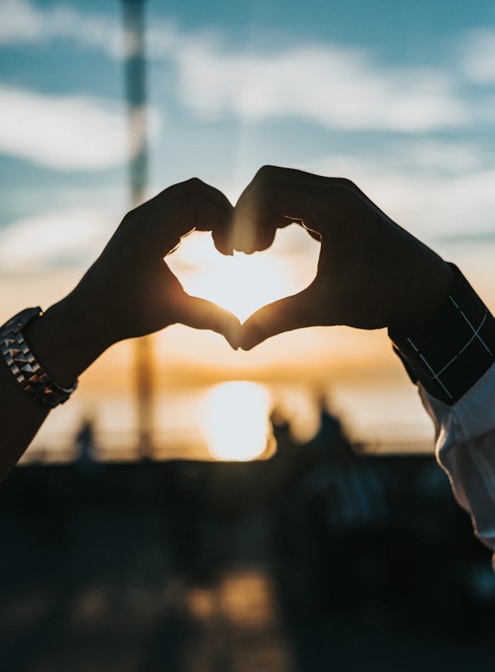 Two hands forming a heart against a sunset
